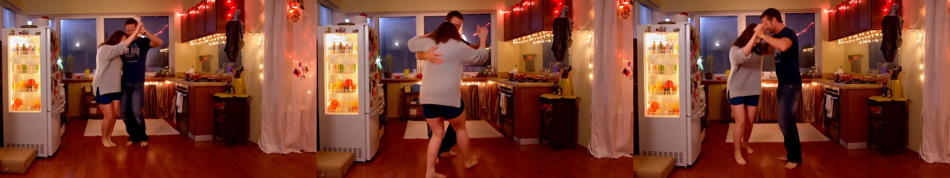 Quattro fotogrammi di una coppia adulta che balla lentamente a piedi nudi in una piccola cucina di notte, lei con un maglione grigio e lui con una maglietta blu navy, con luci a filo e il frigorifero acceso alle spalle.