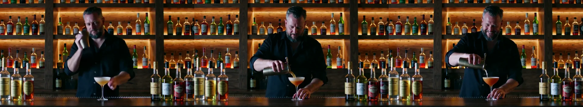 Tre fotogrammi di un barman adulto con una barba grigia curata che agita uno shaker, versa in una coppa e sorride, davanti a uno scaffale di bottiglie illuminato.