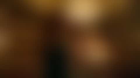 In a gilded Art Nouveau opera box above a packed golden auditorium, a red-haired woman in an emerald velvet off-the-shoulder gown lowers a gold lorgnette and turns to the camera with a slow smile