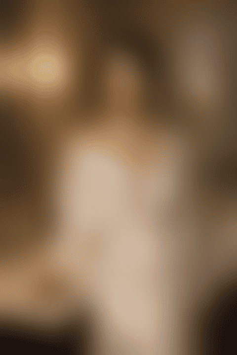 A woman in ivory silk holds a glass of champagne at a marble hotel vanity lit by warm sconces