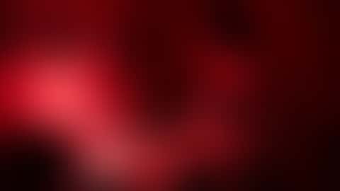 Under a red darkroom safelight, a woman in an open shirt rocks a developer tray, then lifts a dripping print into the light and glances at the camera