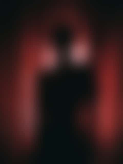 A backlit silhouette turns inside a red velvet stage curtain, the fabric wound across her front and her bare shoulders catching a rim of light