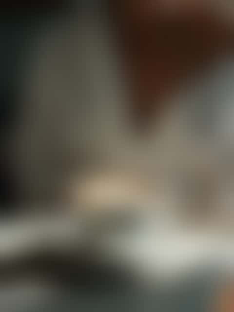 A latte on a sunlit white kitchen counter is lifted out of frame as the camera tilts up to a woman who smiles softly at the viewer