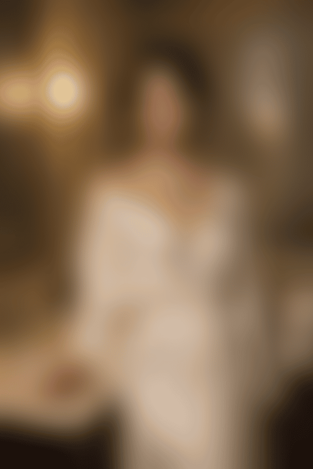 A woman in ivory silk holds a glass of champagne at a marble hotel vanity lit by warm sconces