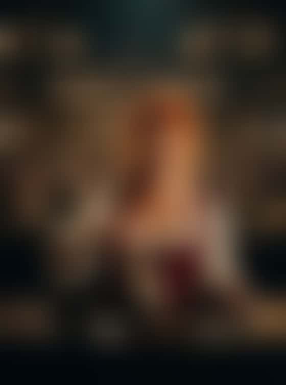 In a candlelit tavern hall lined with barrels and full of drinkers, a red-haired woman in a laced leather bodice drops ice into a horn cup, leans on the bar and runs a fingertip along her bodice