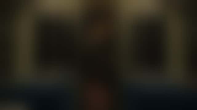 In a dim night train carriage, a woman in a long dark coat with bare legs stands at the door; a man steps in behind her and they end up face to face as tunnel lights strobe