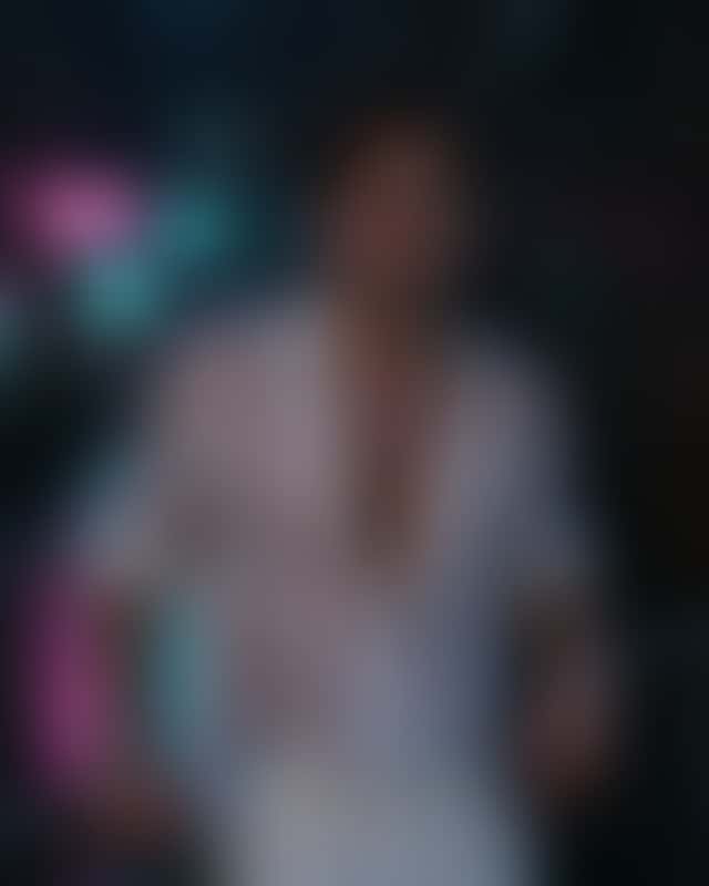 The same man in the same open white shirt and pose, now in a narrow rainy night alley, the shirt soaked against his chest and pink BAR and teal OPEN LATE neon reflected on the wet ground and his skin.