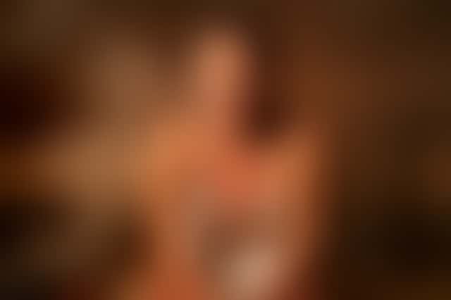 A woman with a towel sits in a wooden sauna, tips a ladle of water onto the stones, vanishes in a burst of steam and wipes her collarbone looking at the lens