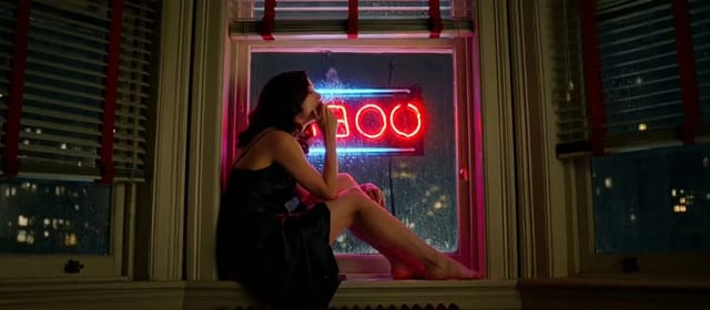 Anamorphic night interior: a woman on an apartment windowsill exhaling smoke against rain-streaked glass under a red neon sign