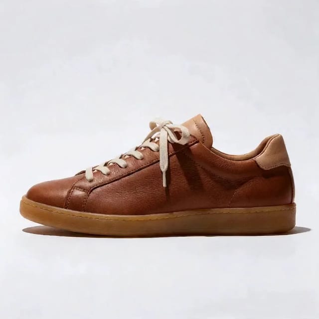 A tobacco-brown leather sneaker with a honey gum sole and cream laces turns on an invisible turntable against a white studio backdrop, moving through side, front three-quarter and top-down views