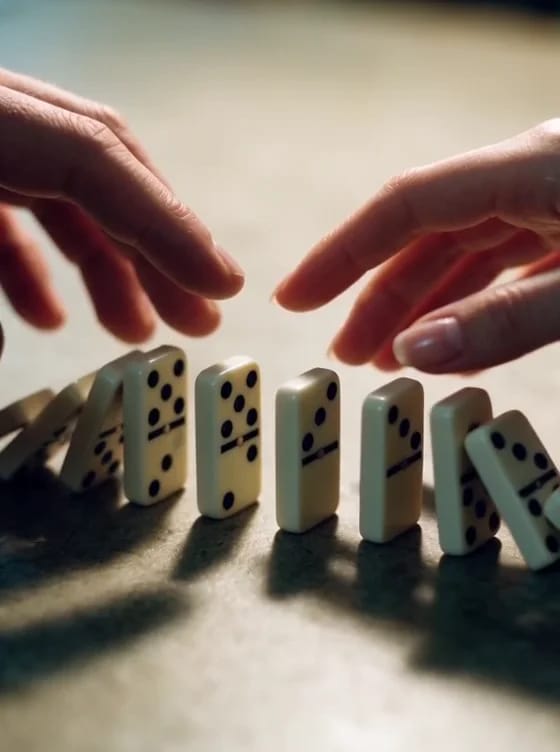 Macro shot of two rows of dominoes falling inward across a table and stopping between a man's hand and a woman's hand that almost touch