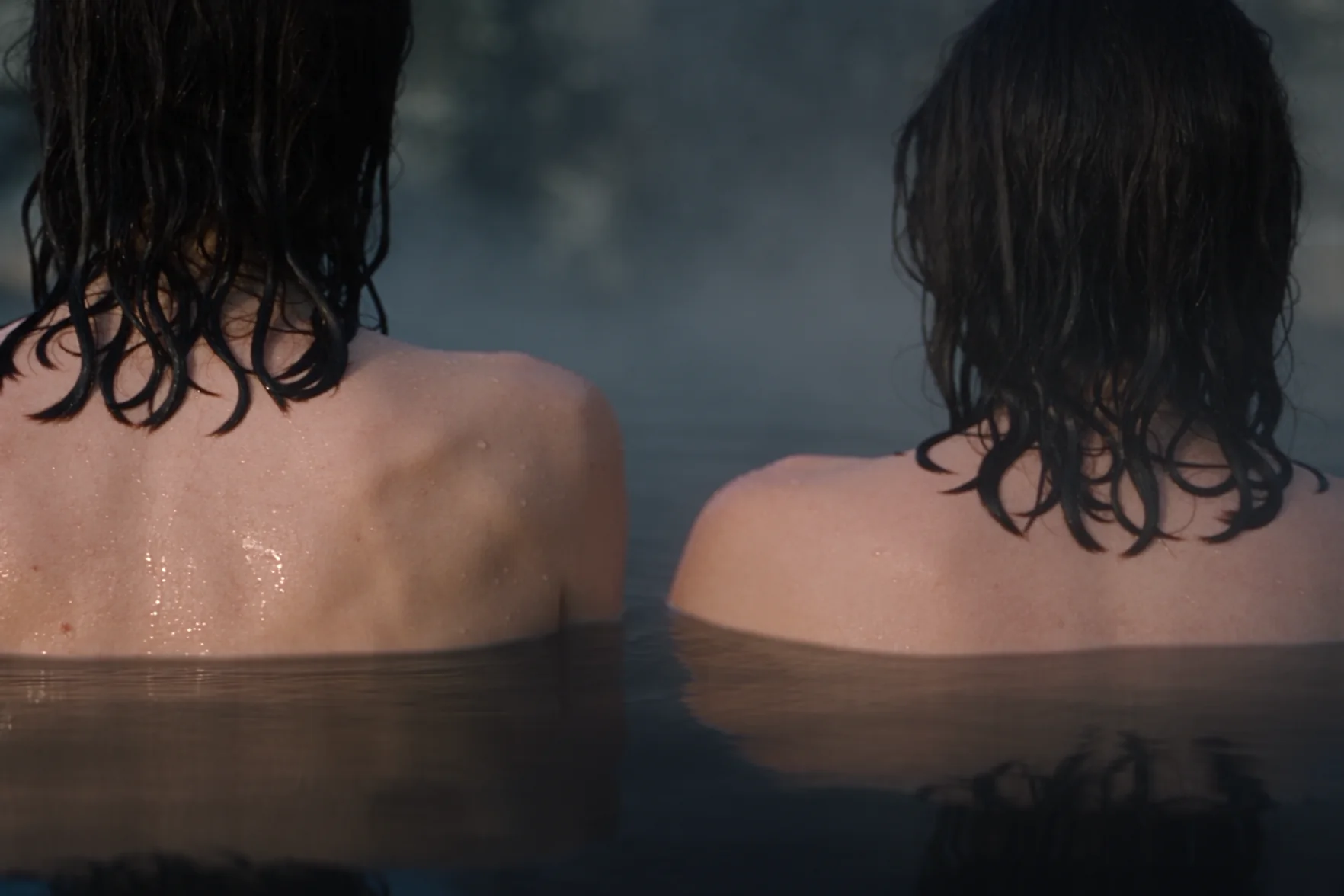 Due donne viste di spalle, con le spalle sopra l’acqua di una sorgente termale all’aperto fumante al crepuscolo